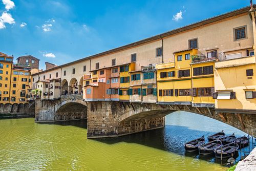 Free Sunny view of Ponte Vecchio, a historic bridge with colorful shops over the Arno River in Florence, Italy. Stock Photo