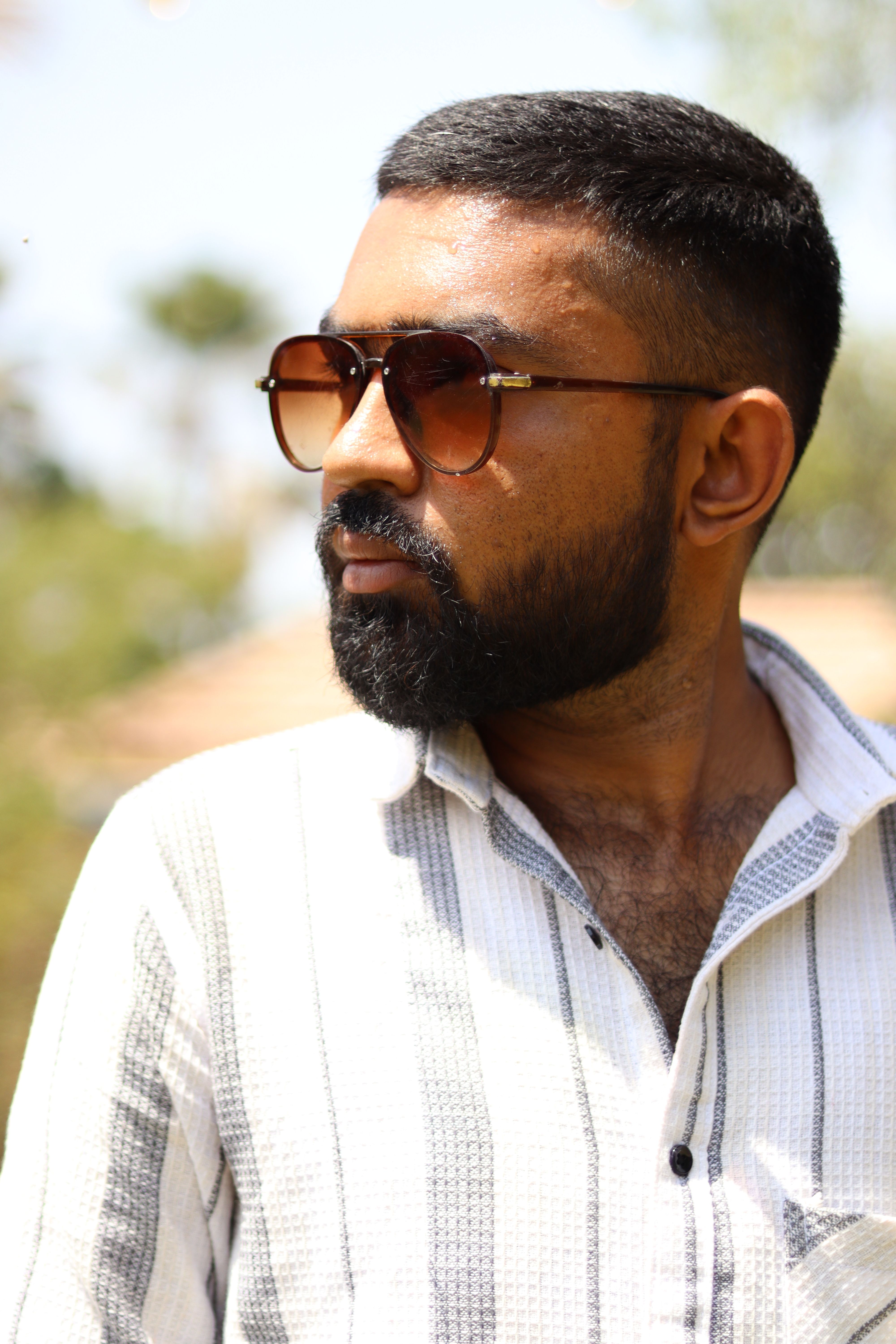 Close-up of a bearded man wearing sunglasses outdoors, conveying a casual and stylish vibe.