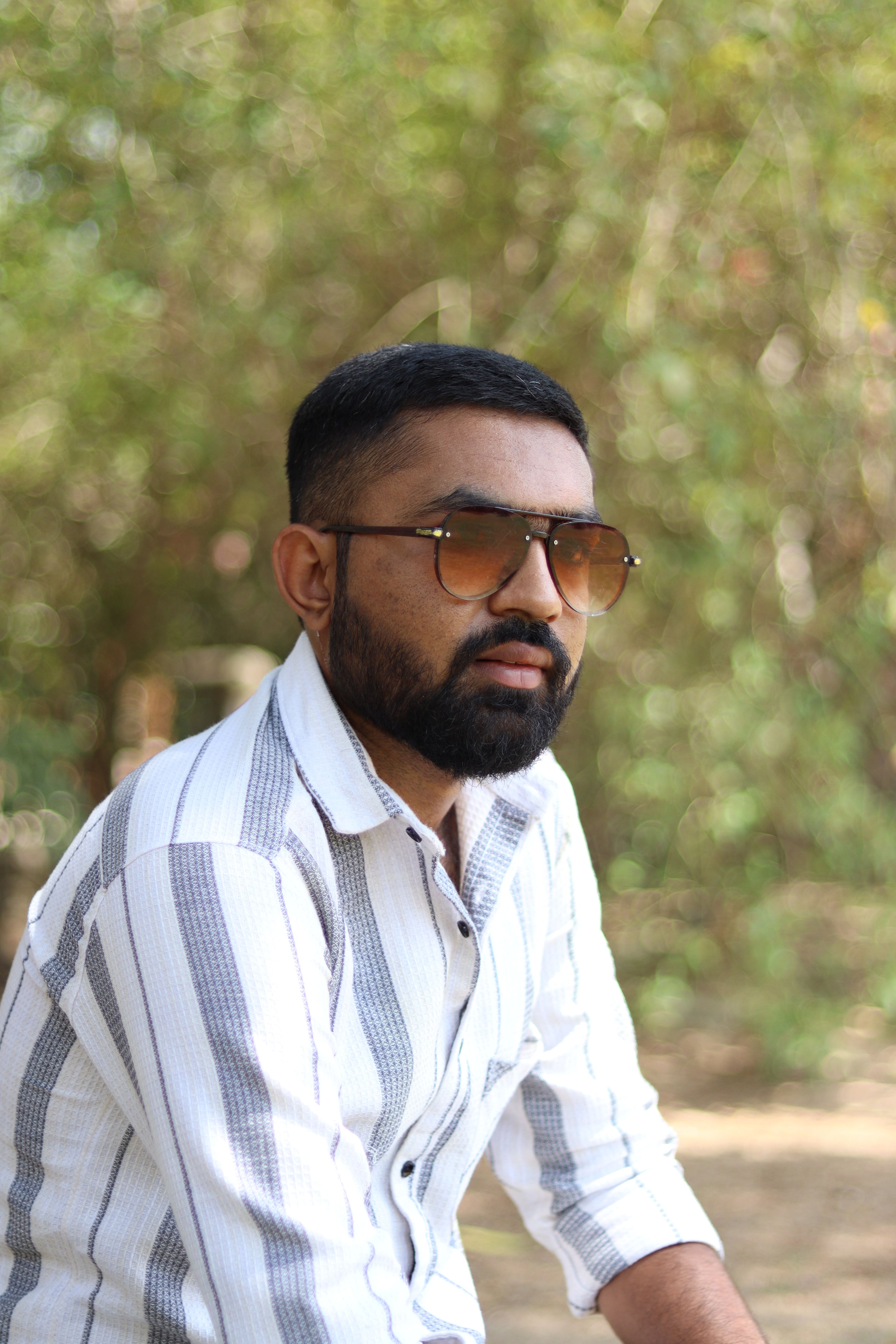 Portrait of a man relaxing in a garden wearing sunglasses and a striped shirt during a sunny summer day.