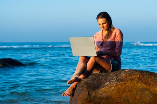 無料 ノートパソコンを使用しながら茶色の岩の上に座っている女性 写真素材
