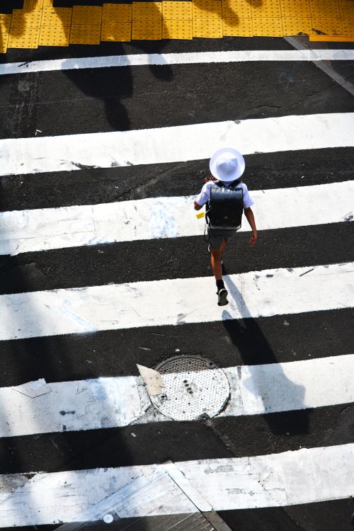 Free Child with backpack crosses zebra stripes in vibrant city scene. Stock Photo