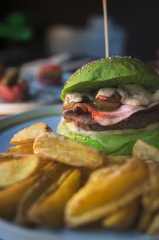 Close-up of a gourmet burger with green bun and crispy potato wedges, perfect for food lovers.