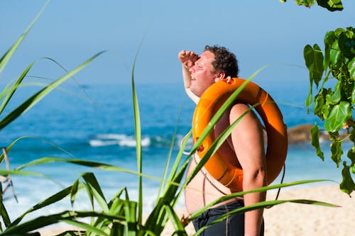 무료 수역 근처의 남자 어깨에 주황색 안전 고리 스톡 사진
