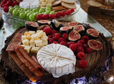 Elegant cheese and fruit platter featuring brie, figs, grapes, and raspberries on a wooden slab.