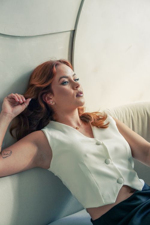 Free Portrait of a relaxed woman with red hair wearing a white shirt, reclining on a sofa indoors. Stock Photo
