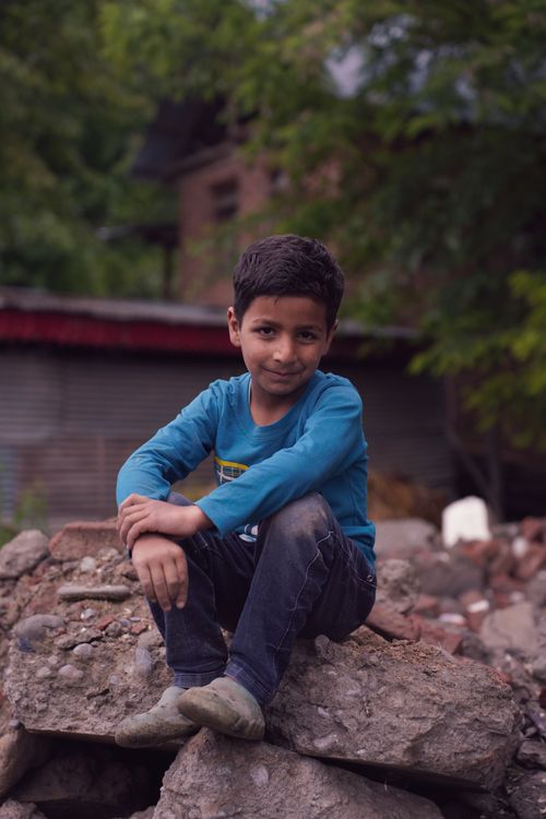 Free A young boy smiling while sitting on rocks outdoors with a natural backdrop, evoking a sense of adventure. Stock Photo