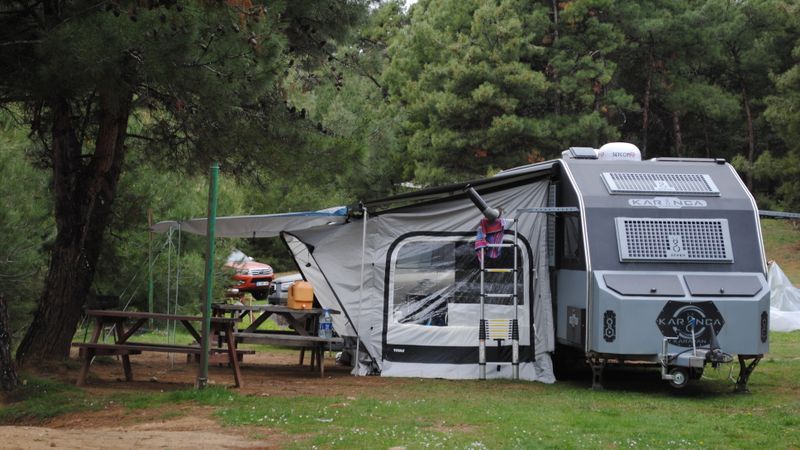 motorhome parked at a forest campsite with a portable solar panel set up on the ground