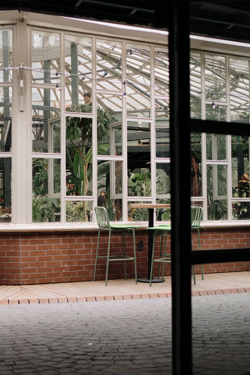Free A cozy café setting inside a glasshouse with lush green foliage visible. Stock Photo