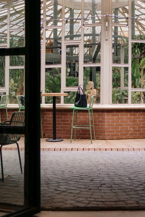 Free A serene scene in a botanical cafe with one person seated at a table, surrounded by lush greenery. Stock Photo