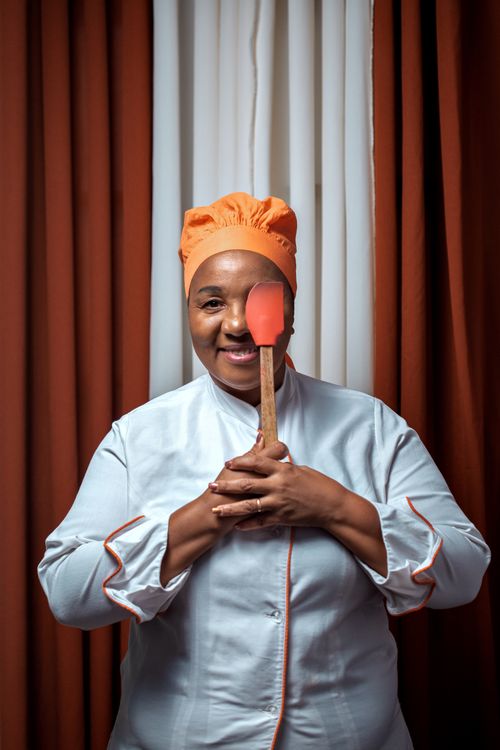 Free Smiling chef in uniform with red spatula against orange curtain background. Stock Photo