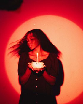 Serene woman holding a candle in dramatic red spotlight, creating a tranquil atmosphere.