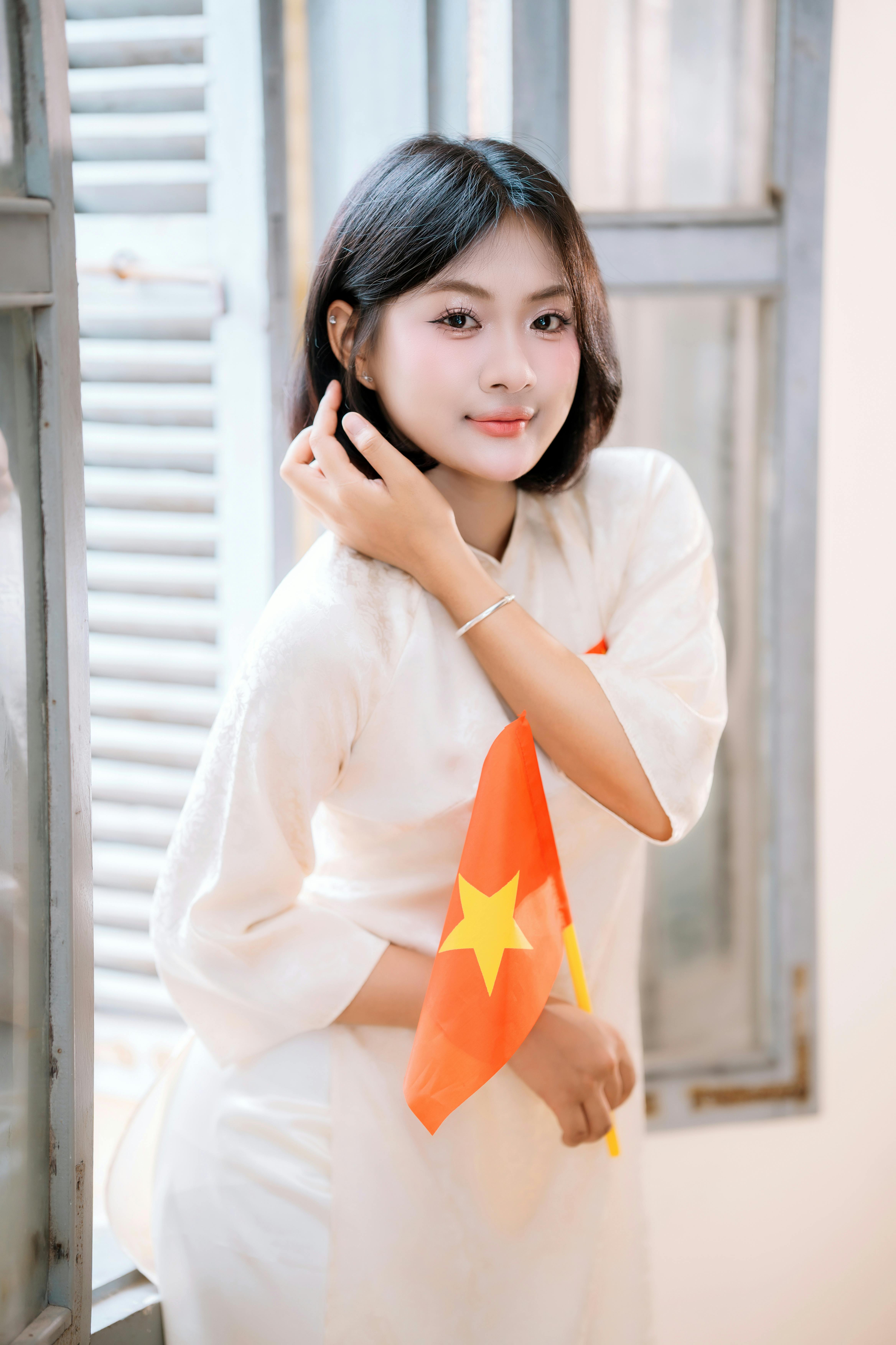 Portrait of a young woman in traditional dress holding a Vietnamese flag indoors.