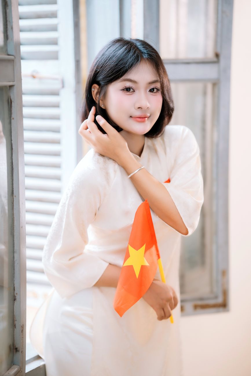 Portrait of a young woman in traditional dress holding a Vietnamese flag indoors.