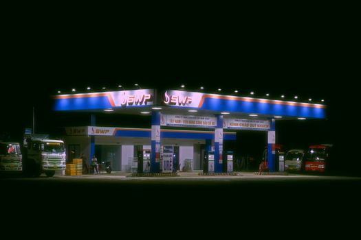 Photo by Vinh Chế Nighttime view of a brightly lit gas station with trucks and cars parked.