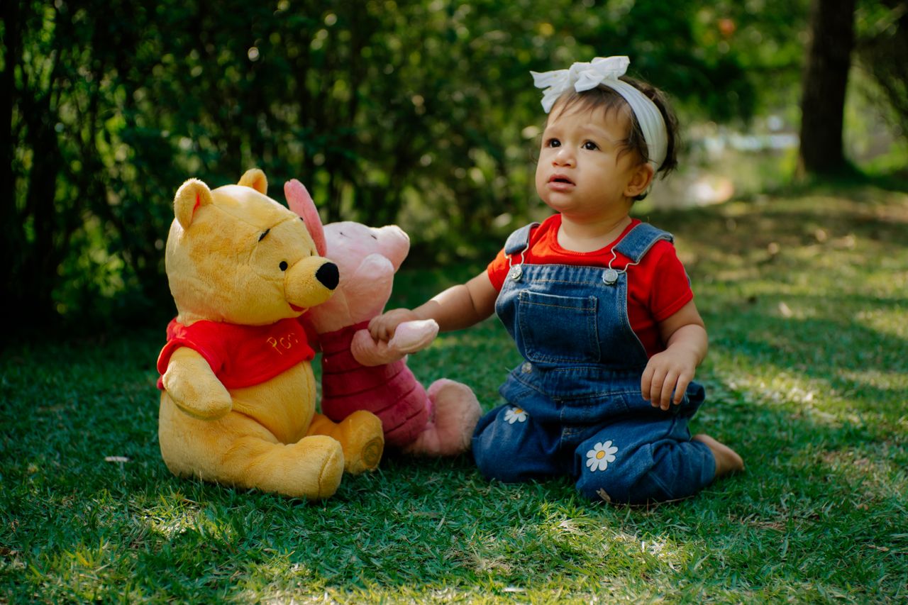 adorable child in denim and red plays with pooh bear plush toys on gra