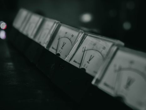 Close-up of vintage analog voltage meters in a dark industrial setting with a moody atmosphere.