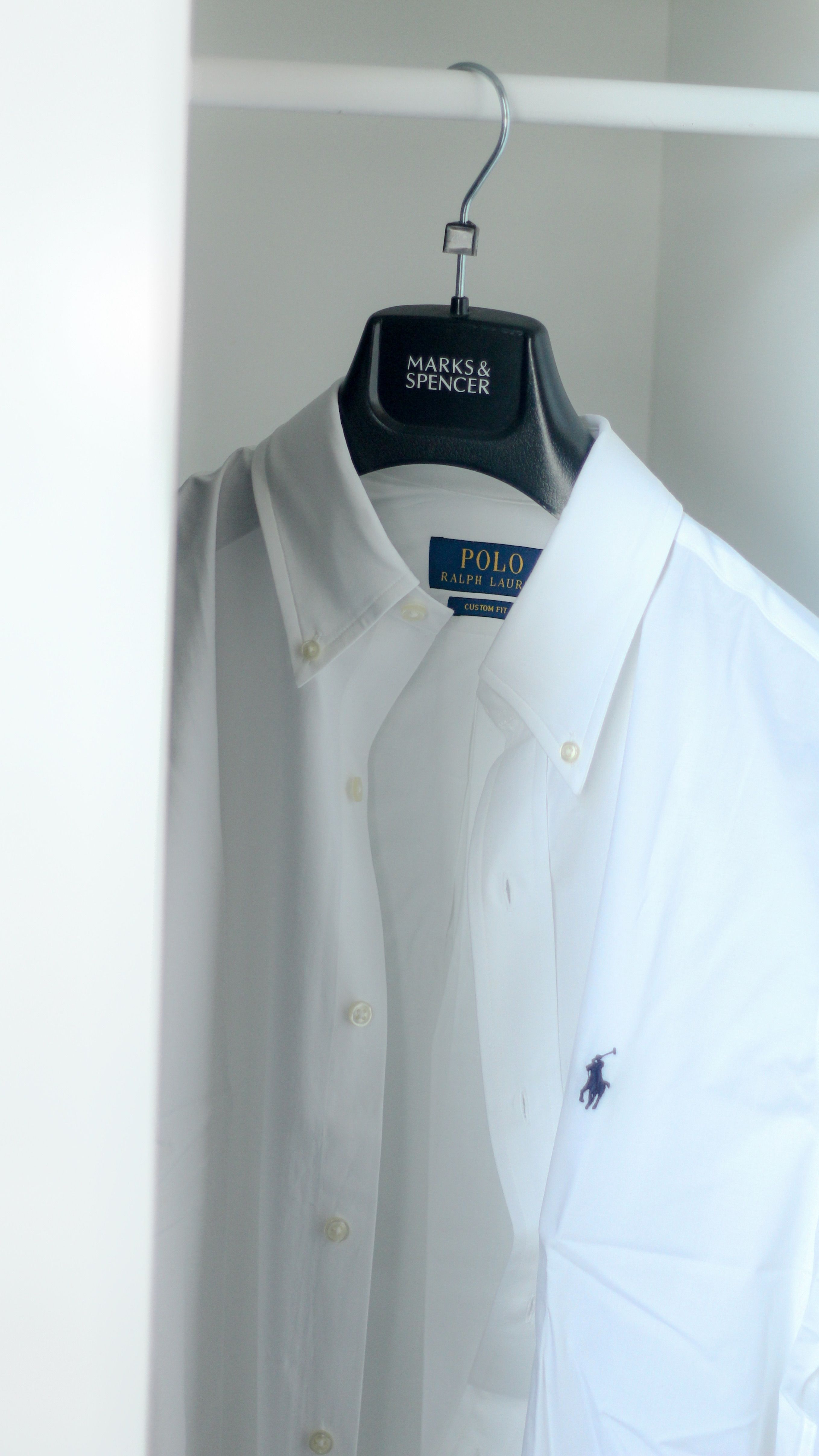 Crisp white Ralph Lauren polo shirt hanging in a modern minimalist wardrobe.