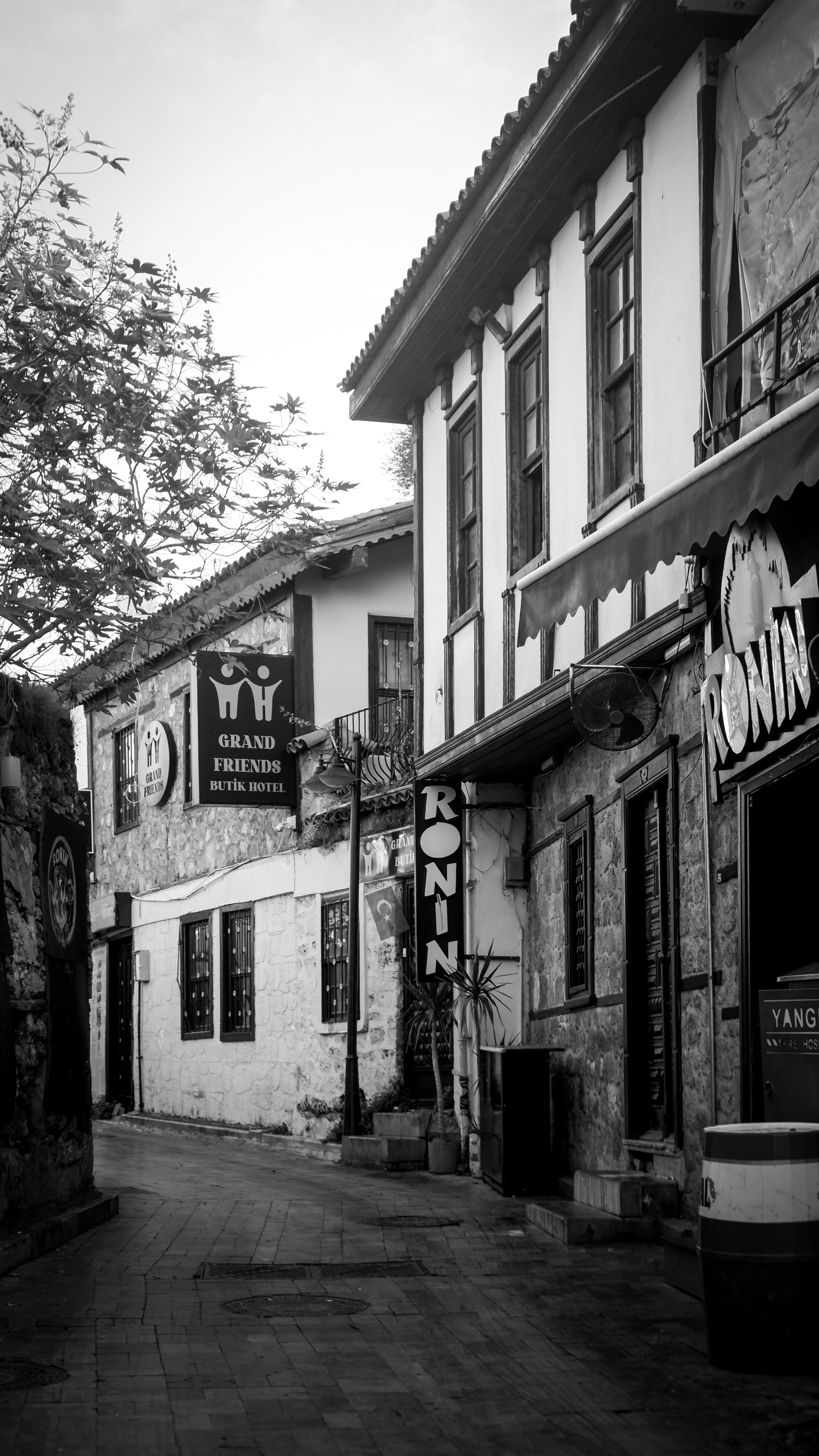 Black and white photo of a quaint narrow alleyway lined with old buildings and signs.