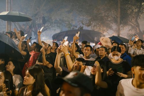 Free A diverse crowd captures a nighttime event using smartphones and umbrellas, creating a lively atmosphere. Stock Photo