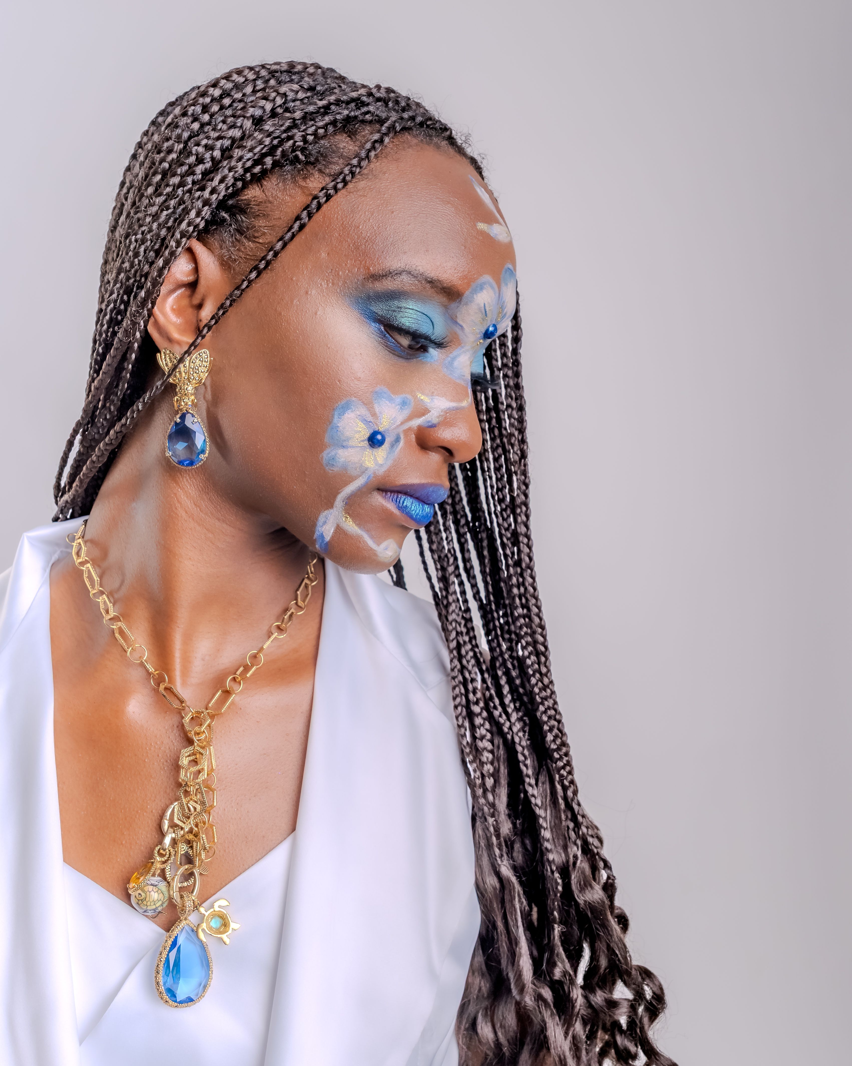 Portrait of a woman in white dress with blue artistic makeup and jewelry, exuding elegance and empowerment.
