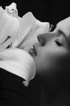 Artistic black and white portrait of a woman with a lily flower, showcasing a delicate pose.