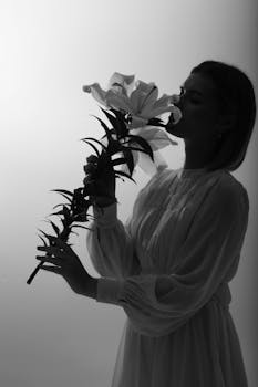 Elegant black and white portrait featuring a woman holding and smelling a lily flower in a studio setting.