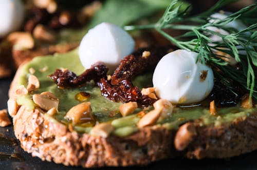 Free Delicious slice of bread topped with avocado, mozzarella, nuts, and sundried tomatoes. Stock Photo
