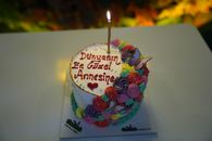 A vibrant and colorful Mother's Day cake adorned with flowers and butterflies, lit by a single candle.