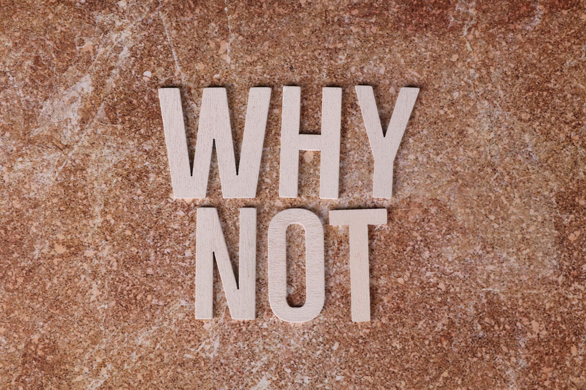 Wooden letters spelling 'WHY NOT' on a textured stone surface background.