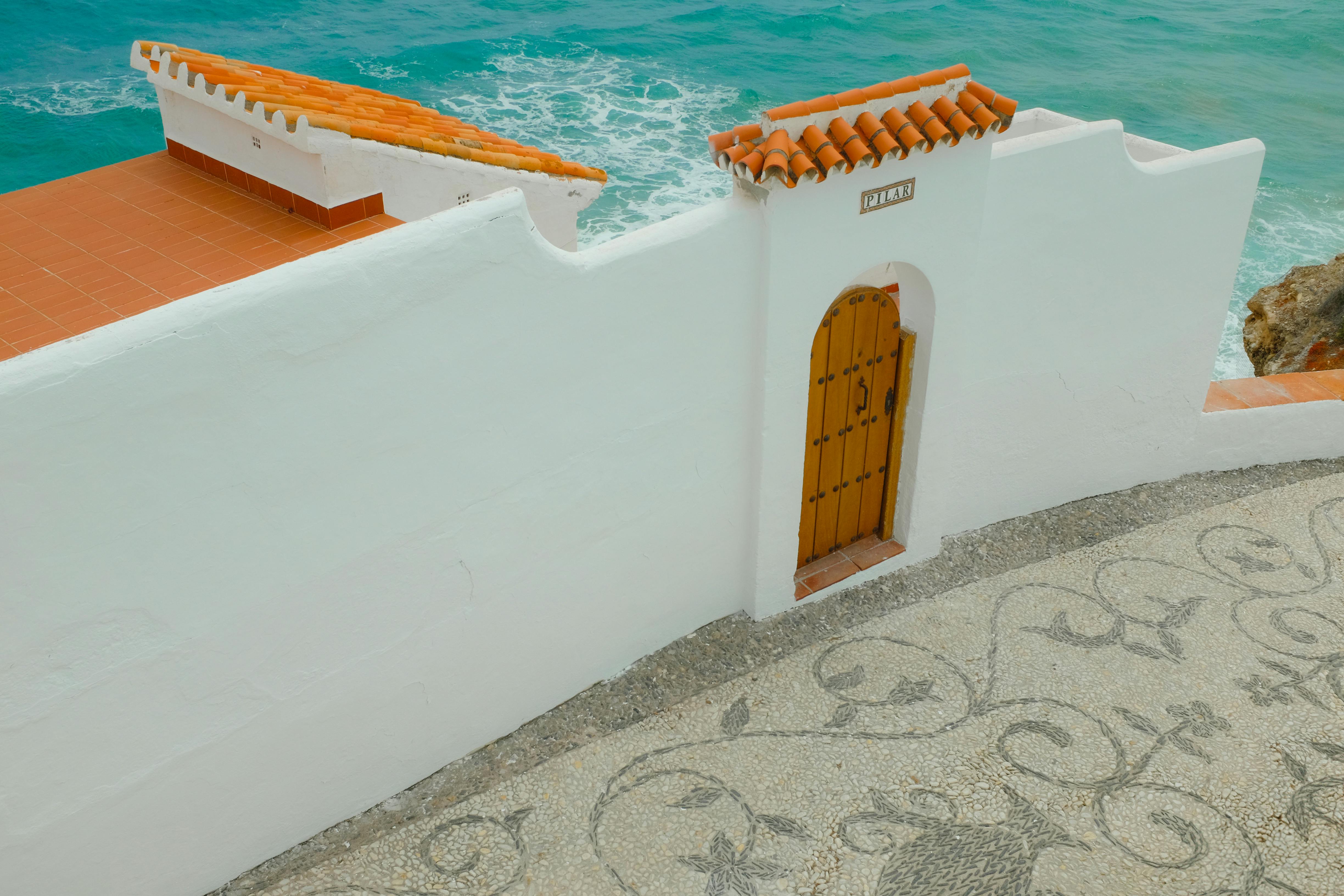 Serene coastal scene with a white wall, wooden door, and turquoise sea, perfect for travel inspiration.