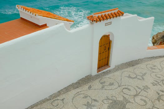 Serene coastal scene with a white wall, wooden door, and turquoise sea, perfect for travel inspiration.
