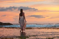 一名女子身穿连衣裙，在充满活力的日落中沿着宁静的海滩散步