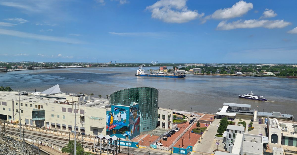 Scenic aerial view of the Mississippi River and New Orleans cityscape with boats and urban buildings.