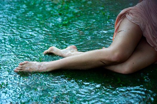 A woman poses with bare legs on wet ground, creating an artistic rain scene.