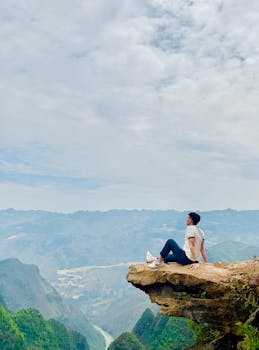 Person sitting on a cliff edge enjoying a breathtaking mountain valley view.