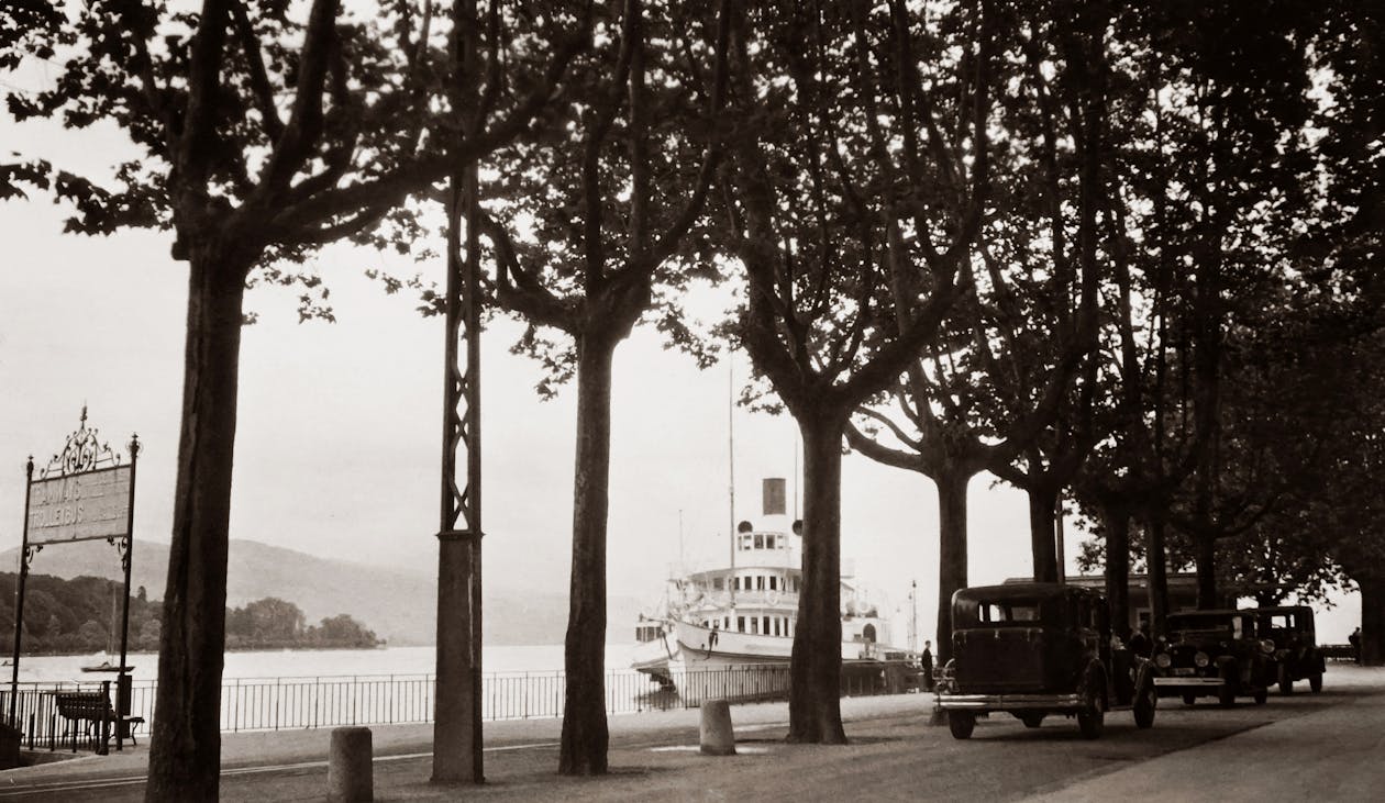 汽车在河边一条街上的老黑白照片，船停靠在码头上