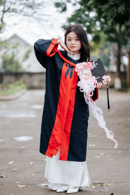 Young woman in graduation gown holding a cap and bouquet, symbolizing success and celebration.