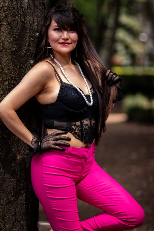 Free Stylish woman in a black lace top and pink pants posing by a tree in a park setting. Stock Photo