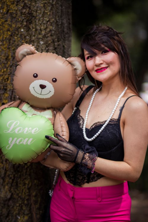 Free Smiling woman with a teddy bear balloon under a tree. Outdoor portrait with a loving theme. Stock Photo