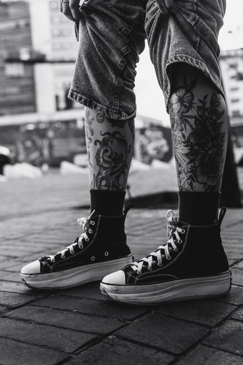 Free Close-up of tattooed legs wearing high-top sneakers in a stylish urban setting. Stock Photo
