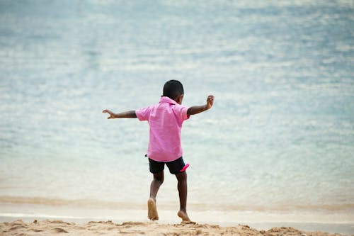 海岸で走っているピンクの襟付きシャツを着た少年