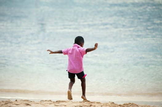 A young boy joyfully playing on a sandy beach with the ocean in the background during a sunny summer day.