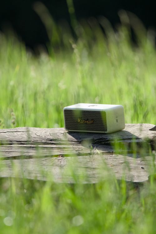 Free A portable speaker resting on a wooden surface surrounded by green grass with sunlight. Stock Photo
