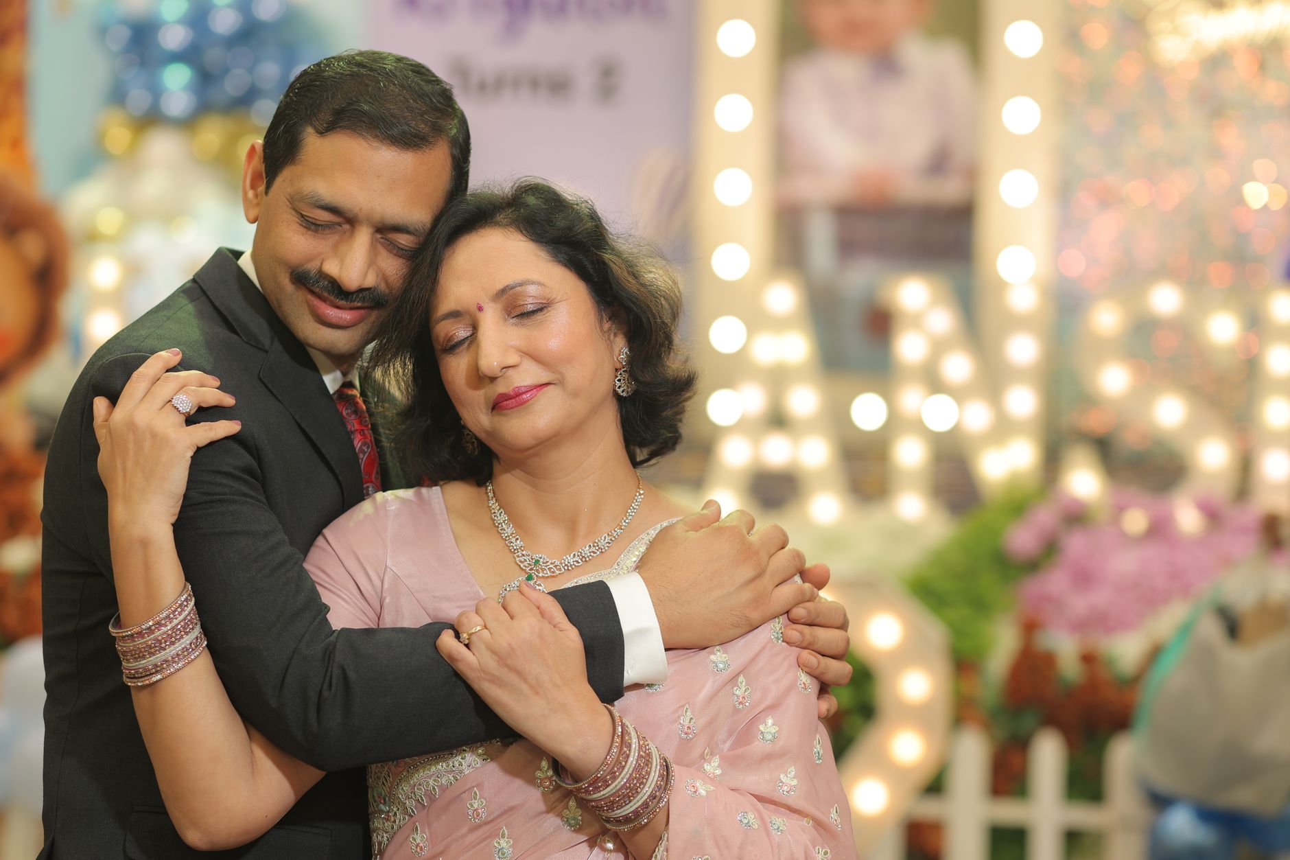 A couple shares an intimate hug at a festive celebration decorated with elegant lights.