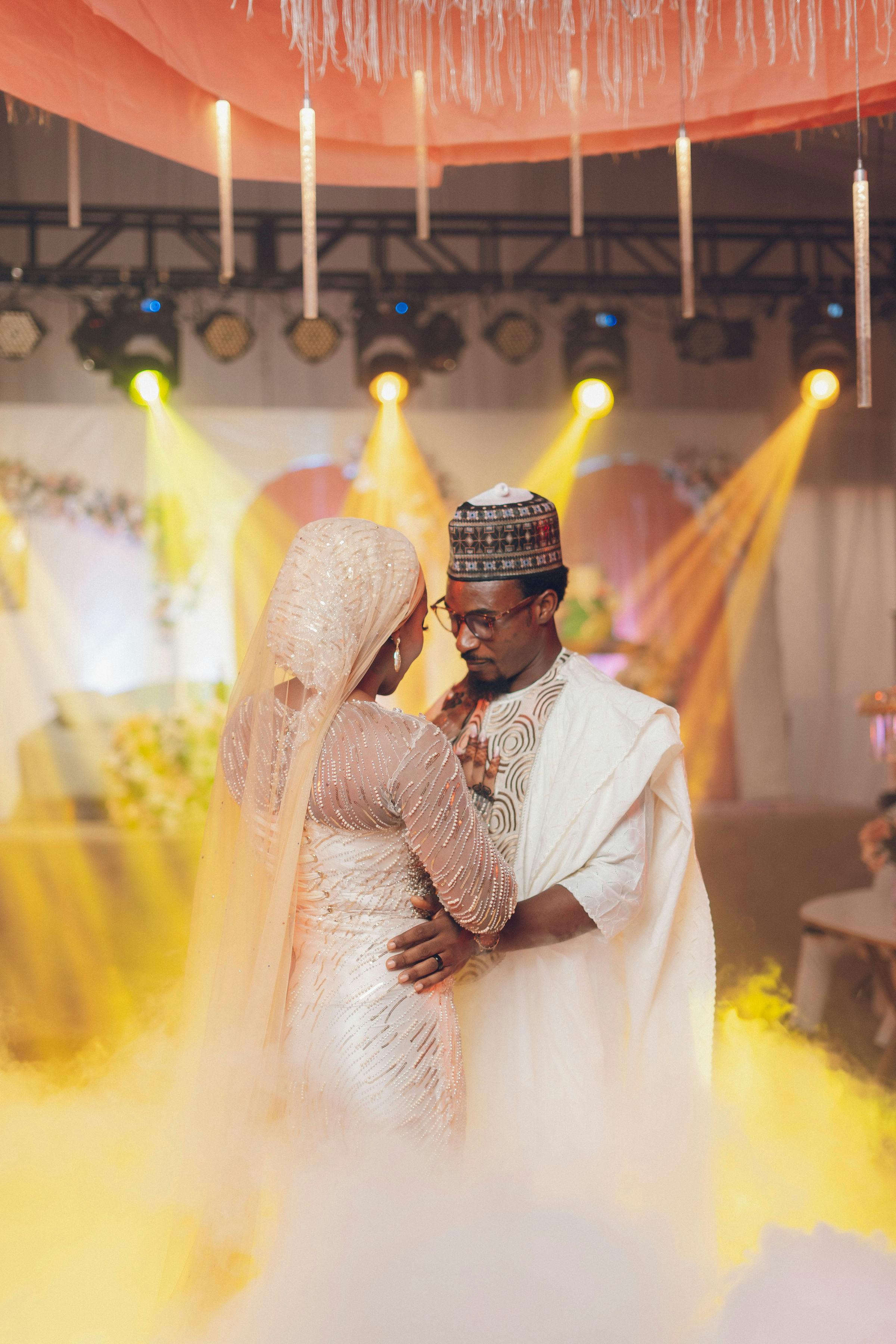 A couple shares a romantic dance at a traditional Nigerian wedding with vibrant lighting.