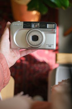 Close-up of a vintage Minolta film camera held indoors with a cozy background.