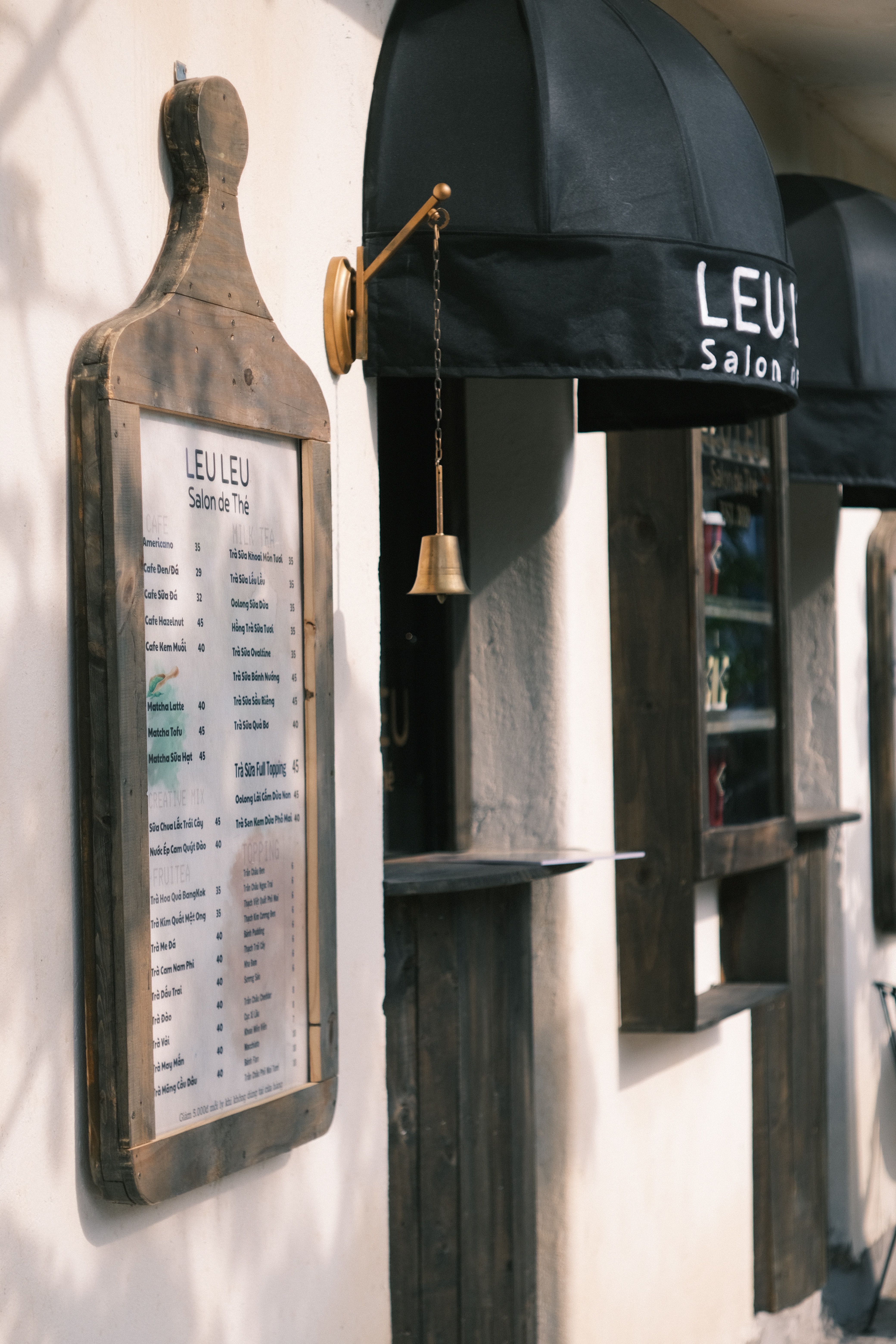 Charming café exterior with a wooden menu board and black awning, creating a cozy vibe.