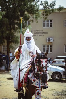 A person dressed in traditional Nigerian attire riding a decorated horse during a cultural festival.
