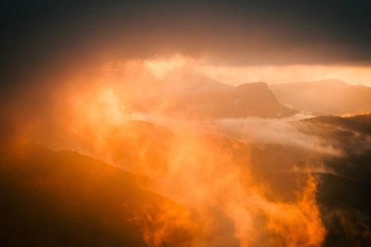 A dramatic view of a glowing sunset casting a warm light over misty mountains.