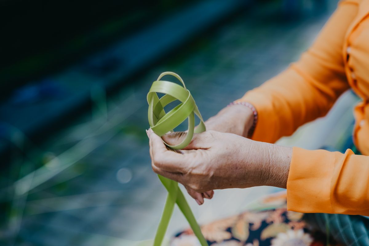 Elderly hands weaving a palm leaf basket by hand
